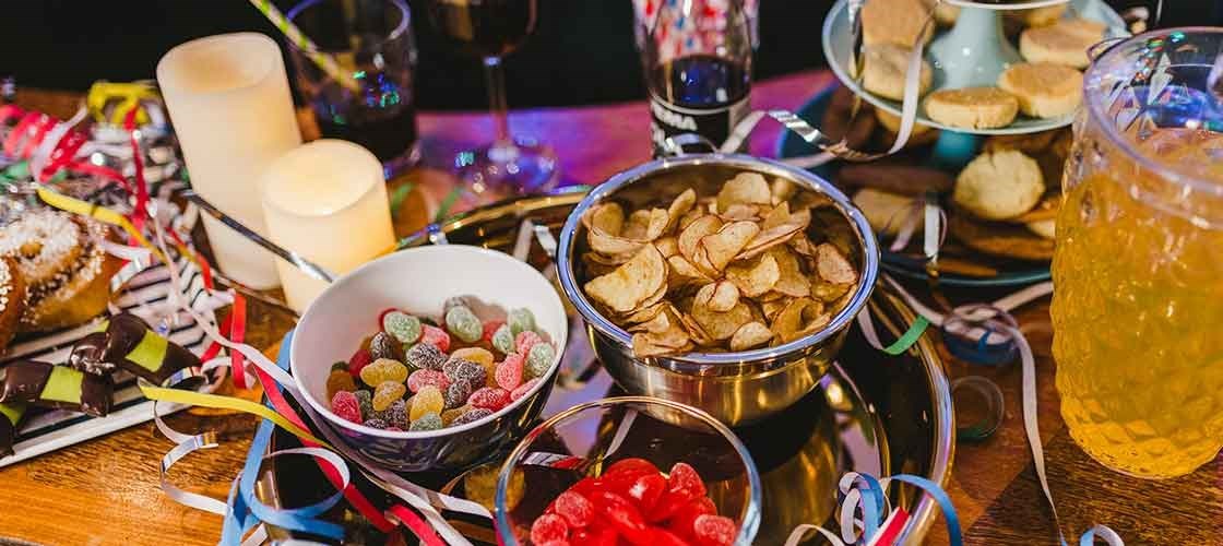 Nyttårsbord med chips, godteri, drikke, lys og fargerike serpentiner.