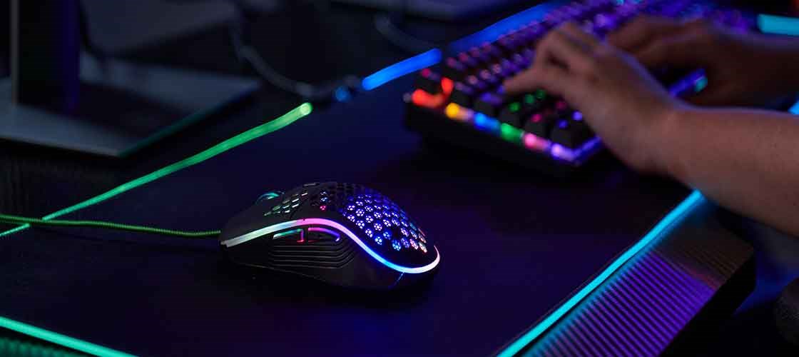 RGB gaming mouse on a desk next to an illuminated gaming keyboard.