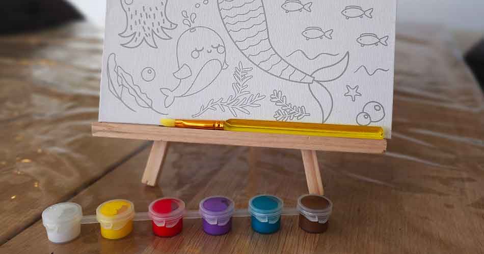 Canvas with a seascape motif, a paintbrush, and paints on a small easel for a creative project.