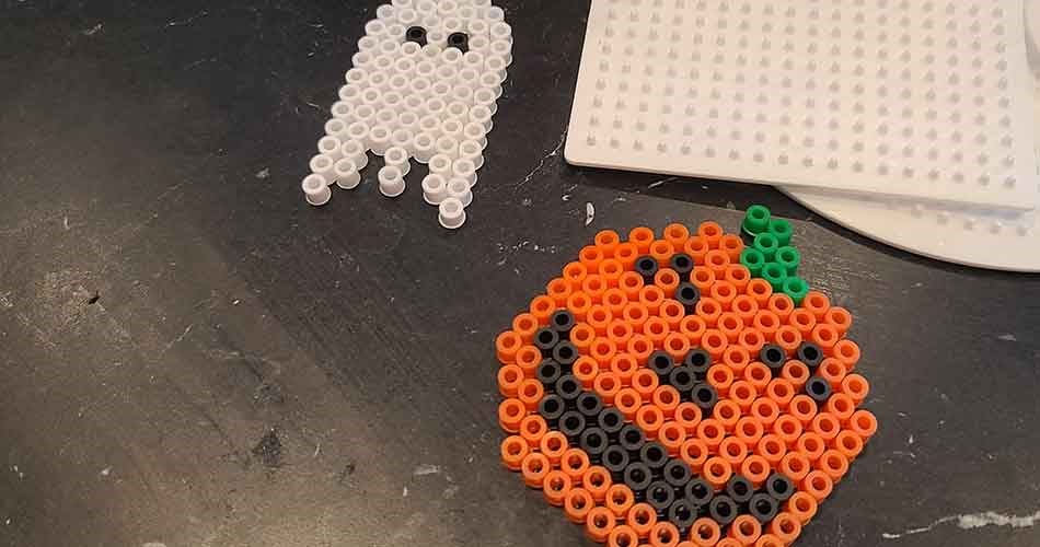 Halloween designs made of beads, featuring pumpkins and ghosts on pegboards.