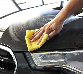 Nærbilde av en hånd som tørker av et svart bilpanser med en gul klut.
