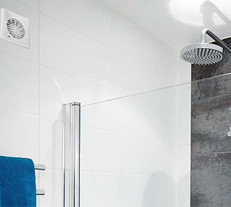 Et flislagt bad med ventilasjonsluke til venstre og dusjhode til høyre. Dusjen har glassdører, og et blått håndkle henger på håndklestativet.