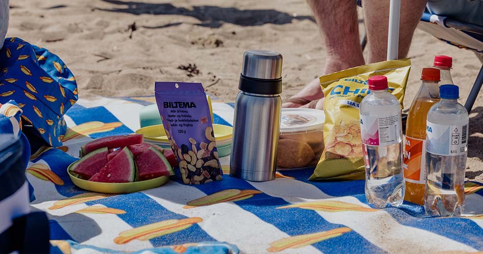 Bildet viser mat og drikke på et strandpledd. 